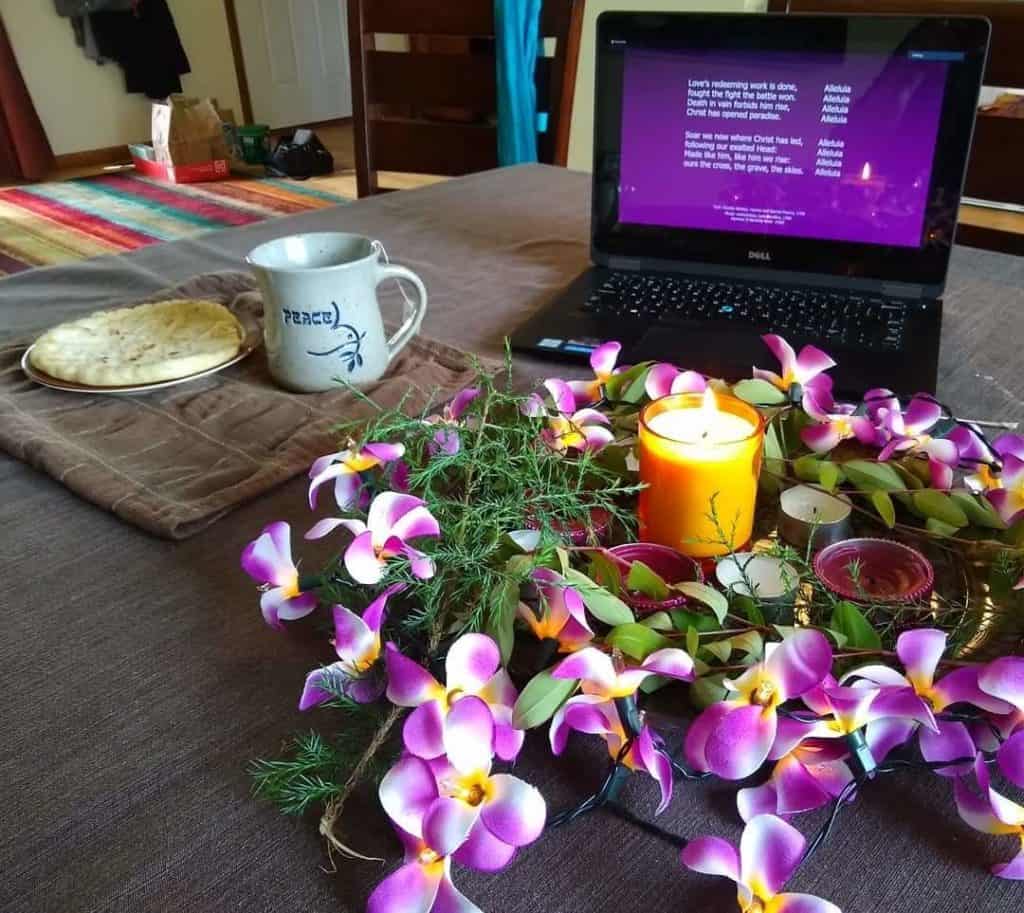 Communion elements, an Easter wreath with flowers and candles, and a laptop in the background.