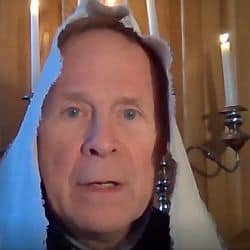 Hans with a scarf over his head and candlesticks behind him.