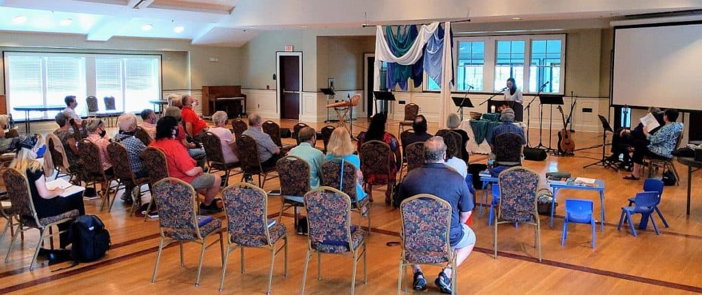 The congregation listens to Melissa preaching up front in the fellowship hall.