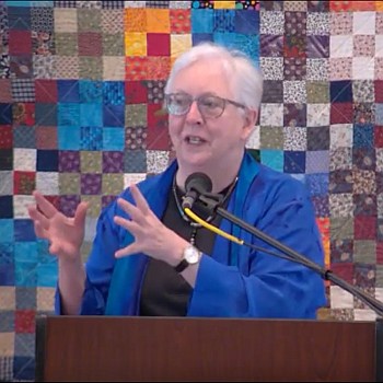 Susan preaching on Oct. 2, 2022 in front of a multi-colored quilt hanging.