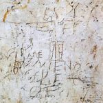 An ancient carving on a wall depicting a man raising his arm to a man with a donkey's head and the saying "Alexamenos adores his god."