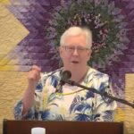 Susan preaching at Raleigh Mennonite in front of a quilted background, Feb. 20, 2023.