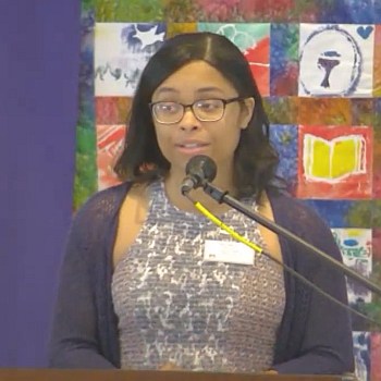 Ren Martin preaching at Raleigh Mennonite on July 15, 2023 in front of a colorful quilted wall hanging.