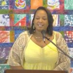 Dr. Candace Laughinghouse speaking at Raleigh Mennonite on Aug. 20, 2023 in front of a colorful quilted wall hanging.