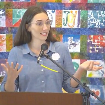 Melissa preaching with her hands held out, illustrating a point, on Sept. 3, 2023 in front of a multi-colored quilted wall hanging.
