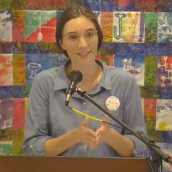 Melissa with her fingers interlaced behind a quilt background