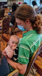 A baby sits on the lap of his father during worship service at Raleigh Mennonite. Other folks can be seen sitting in the background.