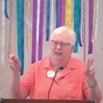 Susan holding up her hands with "air quotes" while preaching on June 23, 2024