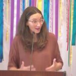 Raleigh Mennonite Church Melissa preaching in front of a ribbon banner.