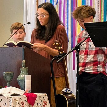 Jude, Melissa and Wick behind a podium with Melissa reading a prayer.