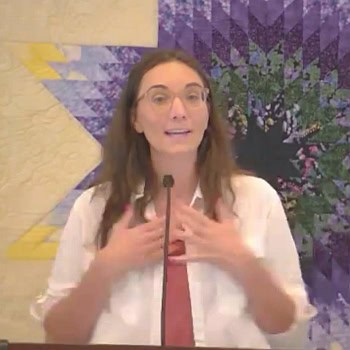 Melissa preaching at RMC on Sept. 15, with her hands tapping her chest, in front of a colorful purple and yellow star-shaped quilt.