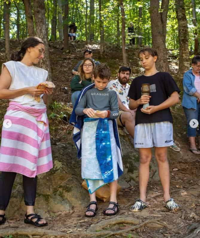 Three people standing on the side of a hill with towels wrapped around them, preparing to serve communion to others.