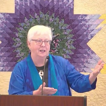 Susan holding out a hand while preaching in front of a purple star-shaped quilt on Nov. 3, 2024