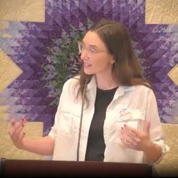 Melissa preaching on Nov. 17, 2024, holding her hands out a bit, looking to her right, while standing in front of a purple and yellow star-shaped quilted wall hanging.