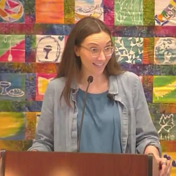 Melissa preaching on Jan. 26, 2025 in front of a colorful banner quilt.