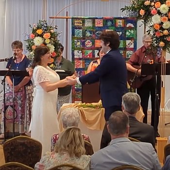 Woman and man in wedding attire dancing to the Servant Song with singers in the background.