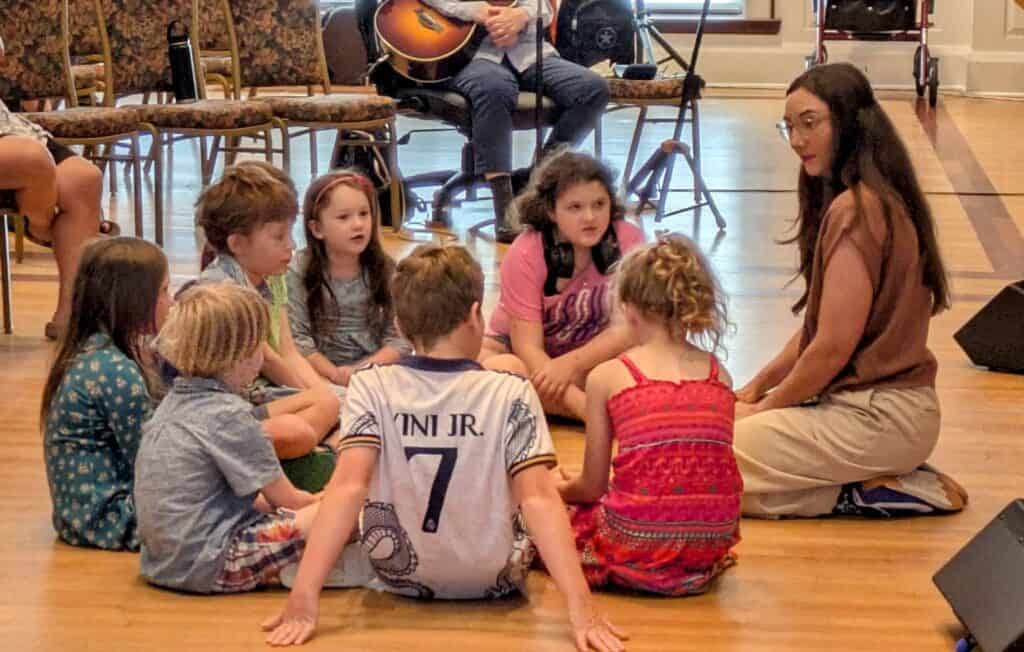 Melissa on her knees in the front of the church speaking with a group of children.