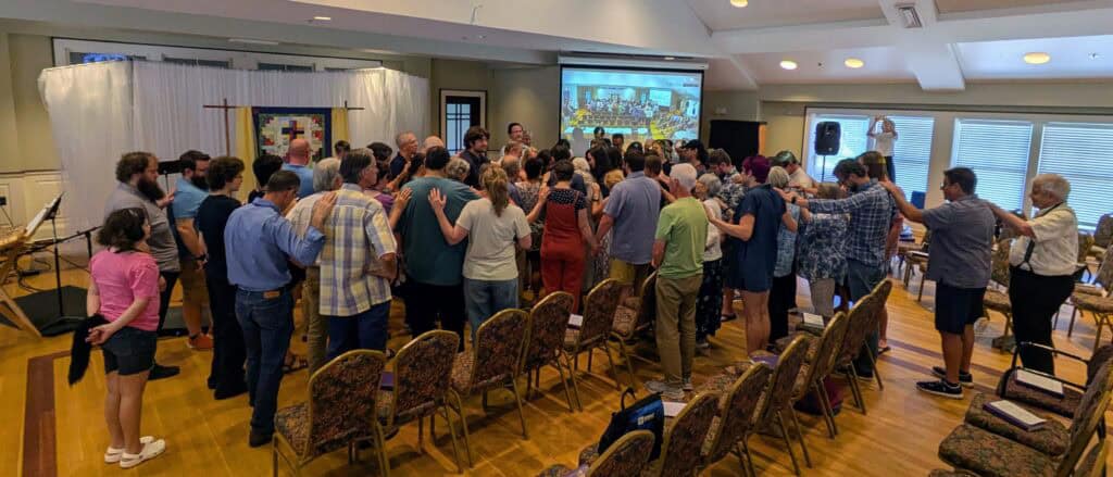 Large group of people surround Melissa as she receives a prayer of dedication.