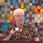 Susan preaching at RMC on Nov. 16, 2025 in front of a colorful quilt.
