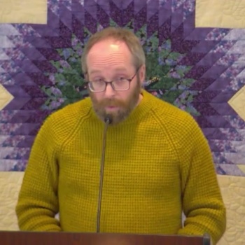 Phil preaching on Jan. 11, 2026 in front of a yellow and purple quilted wall hanging.