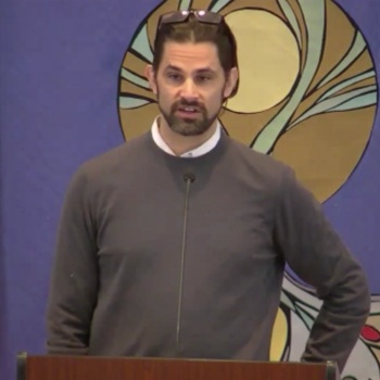 Seth preaching in front of a banner showing a flower emerging from a bulb.