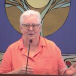 Susan preaching at RMC in front of a blue banner showing a shoot of a plant sprouting.