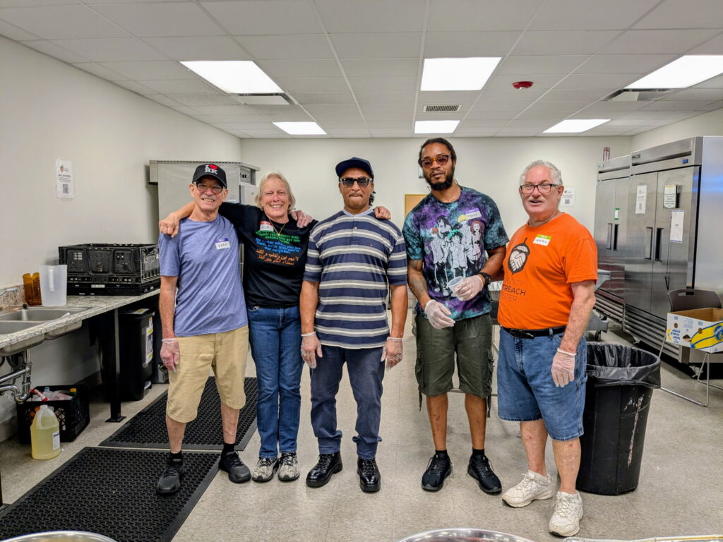 Six people wearing plastic serving gloves in an industrial kitchen.